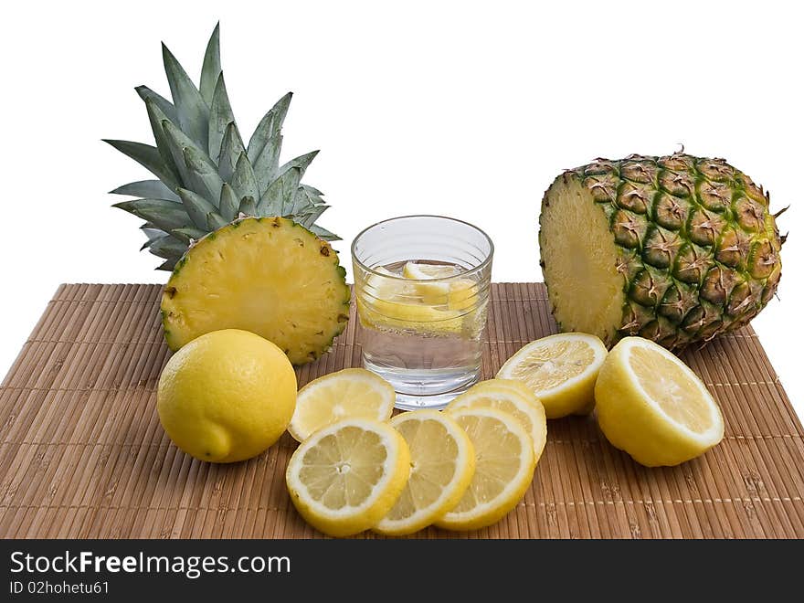 Pineapple with lemons and glass on bamboo mat isolated on white