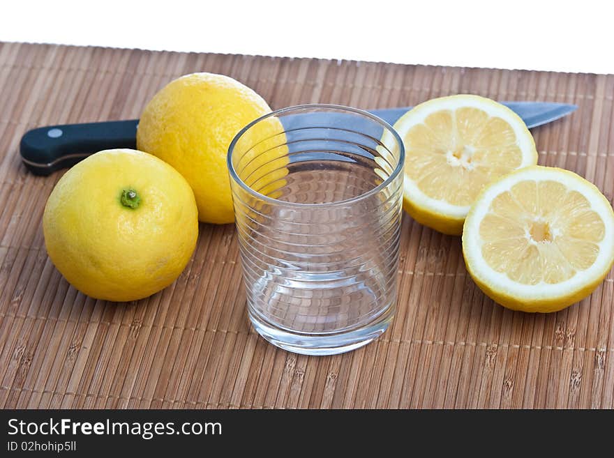 Lemon fruits with kitchen knife and glass on bamboo mat isolated on white. Lemon fruits with kitchen knife and glass on bamboo mat isolated on white