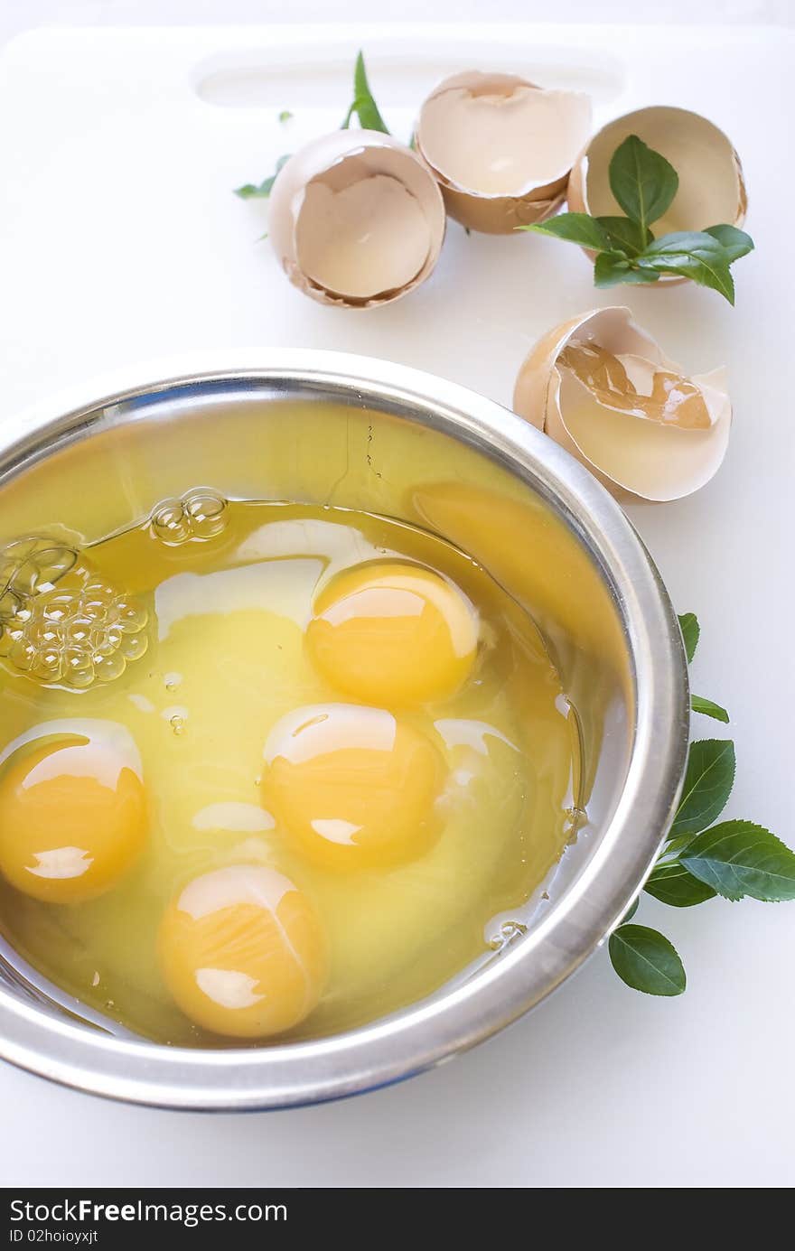 Eggs in the metal bowl with leafs on white cutting board