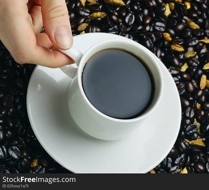 Coffee cup in hand over coffee beans background with cardamom addition