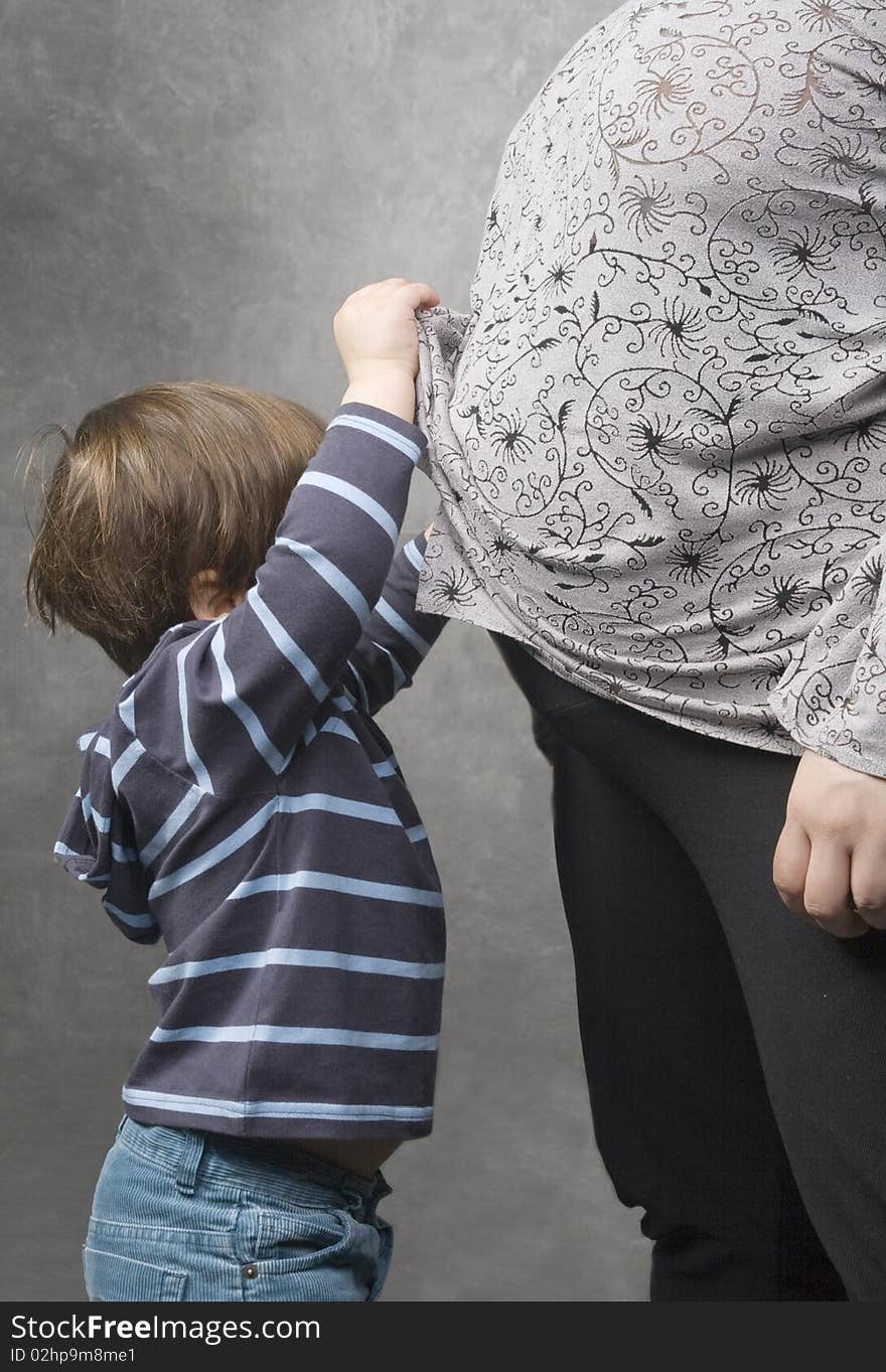 Little boy peeping under his pregnant mother's blouse. Little boy peeping under his pregnant mother's blouse