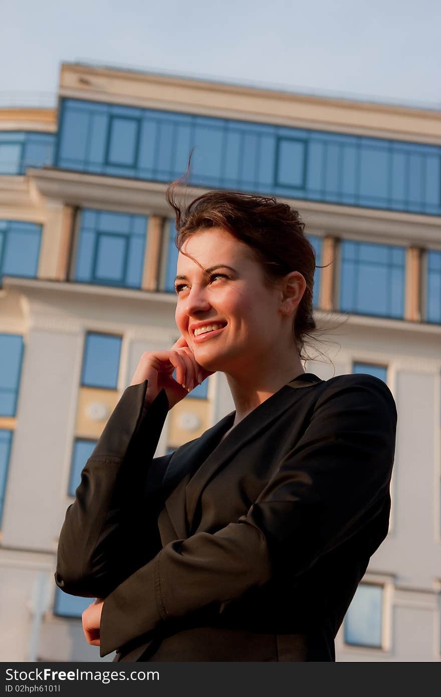 Young smiling businesswomen in black coat in fromt of glassy businesscenter