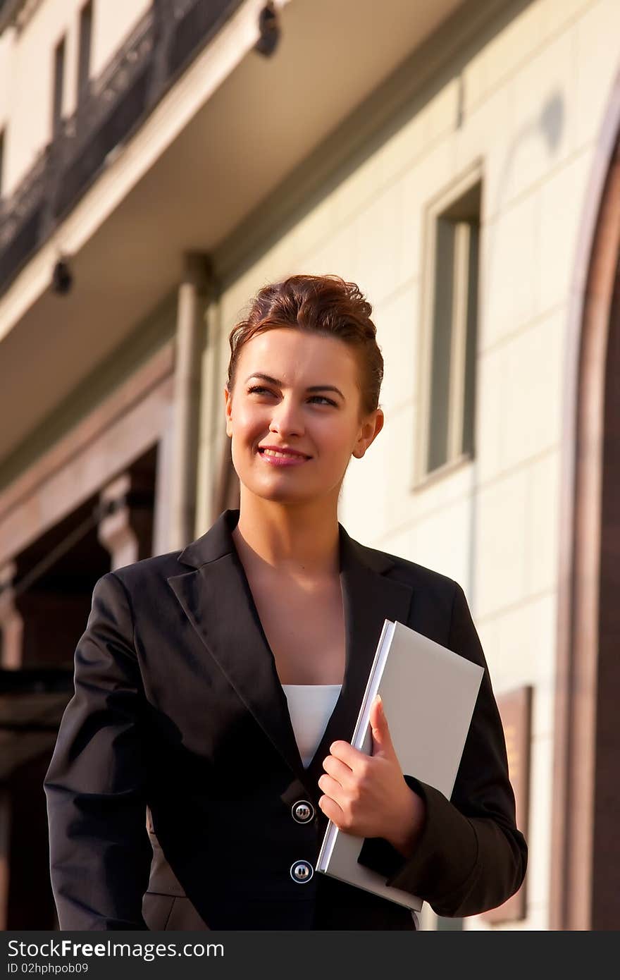 Young smiling businesswomen in black coat passing near businesscenter