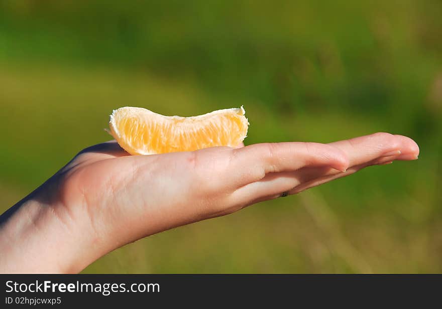 Segment of a juicy orange on a hand of the young girl