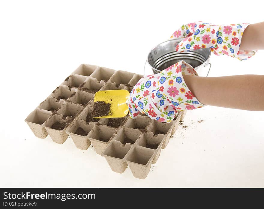 Gardener wearing colorful flower patterned  gardening gloves is using a yellow shovel to place soil from a silver pail into eco-friendly Composted Cow Manure Pots used for transplants- environmentally responsible seed starters. isolated on white 6200. Gardener wearing colorful flower patterned  gardening gloves is using a yellow shovel to place soil from a silver pail into eco-friendly Composted Cow Manure Pots used for transplants- environmentally responsible seed starters. isolated on white 6200