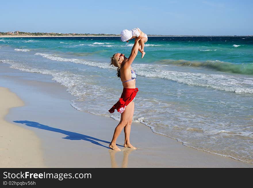 Charming little happy girl laughing in the arms of his mother, against the blue sky on the beach