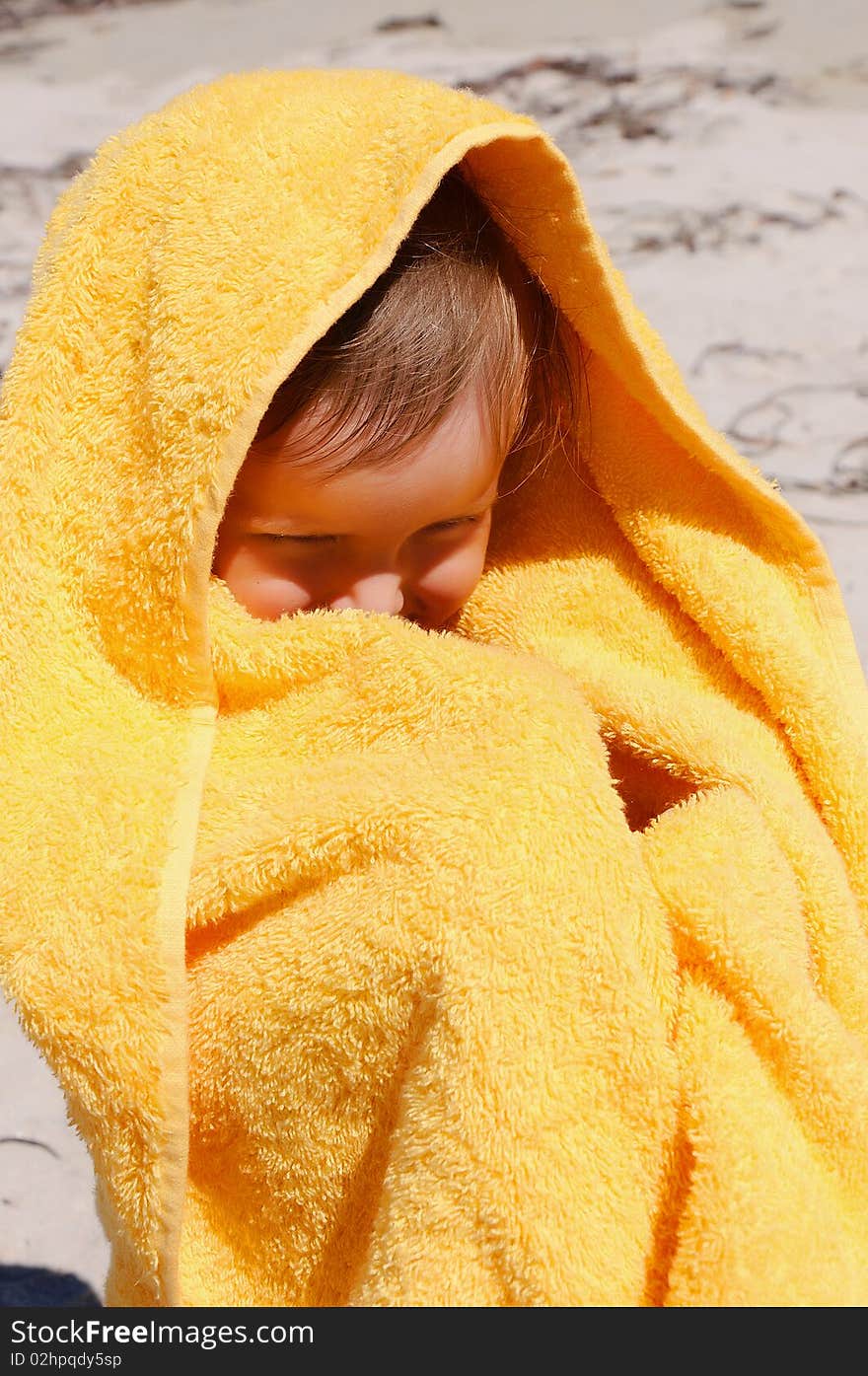 Charming little girl in a yellow towel on the beach as a symbol of childhood happiness and joy