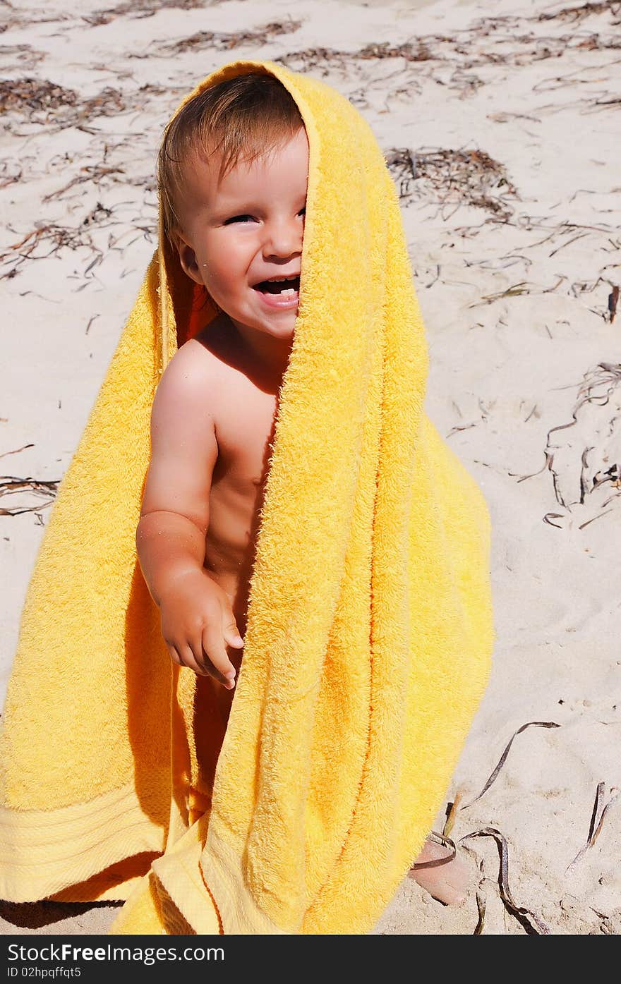 Charming little girl in a yellow towel on the beach as a symbol of childhood happiness and joy