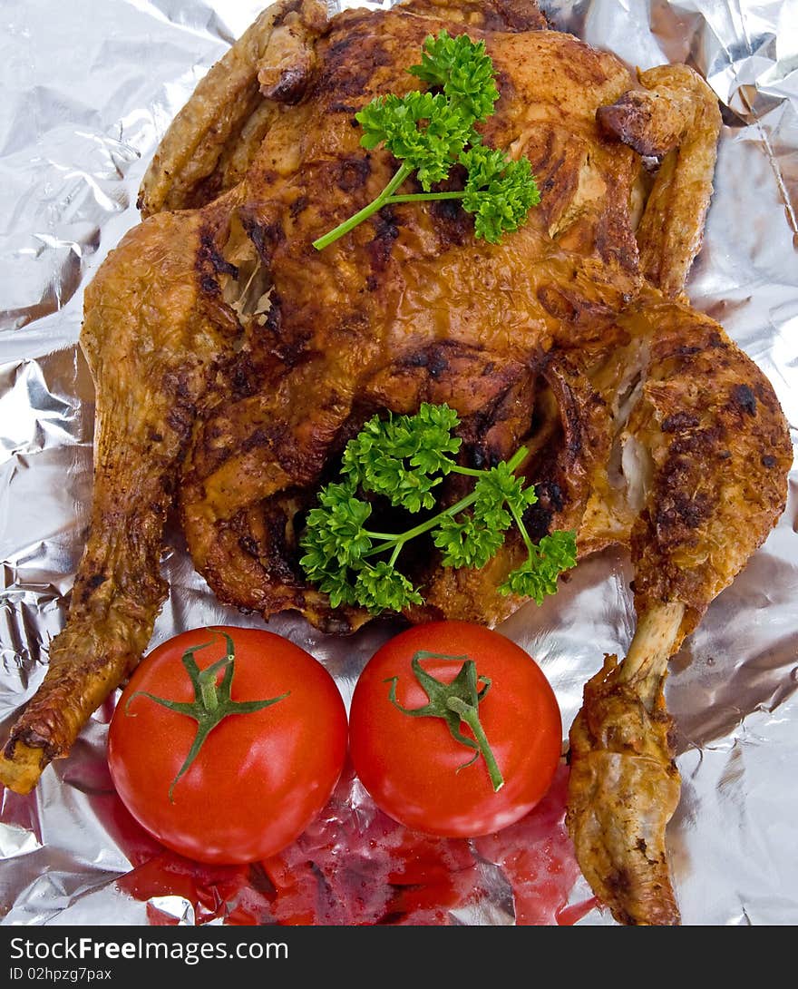 An image of a freshly roasted, spiced, organic chicken with tomatoes and parsley shown on silver foil. An image of a freshly roasted, spiced, organic chicken with tomatoes and parsley shown on silver foil.