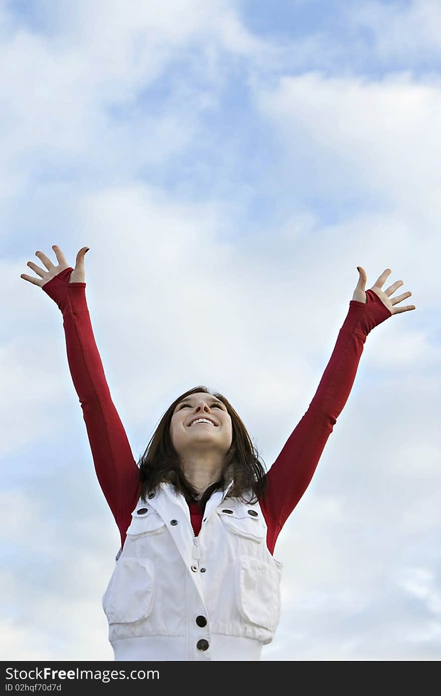 Female wearing red shirt and white vest, reaching both arms up to a blue cloudy sky. Female wearing red shirt and white vest, reaching both arms up to a blue cloudy sky