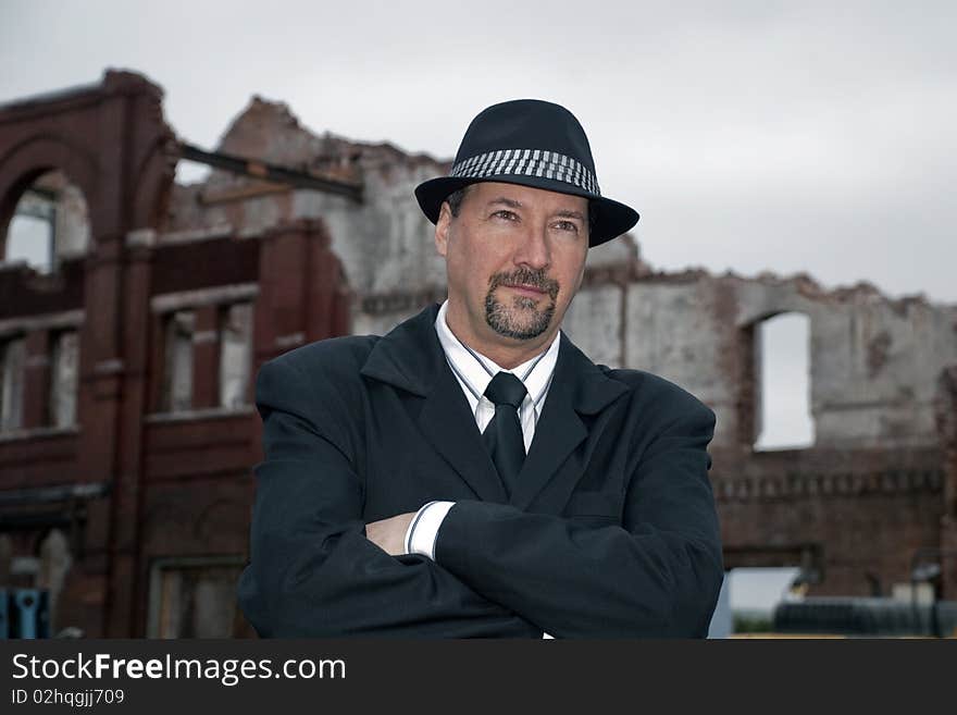 Business man wearing a suit and hat, with his arms folder. a middle aged man with a beard and mustache standing in front of an old brick building ruins. light shy. Business man wearing a suit and hat, with his arms folder. a middle aged man with a beard and mustache standing in front of an old brick building ruins. light shy.