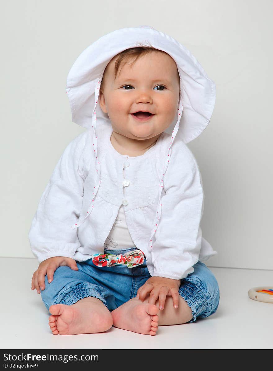 7 month old baby sitting with toy dressed in jeans and jumper