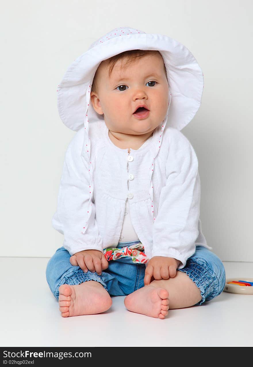 7 month old baby sitting with hat dressed in jeans and jumper