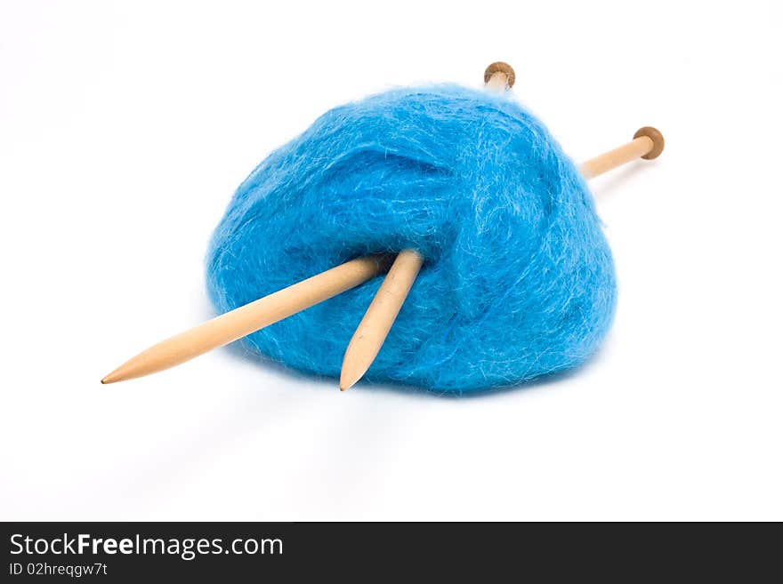 A large ball of blue mohair wool pierced with large wooden knitting needles against white.