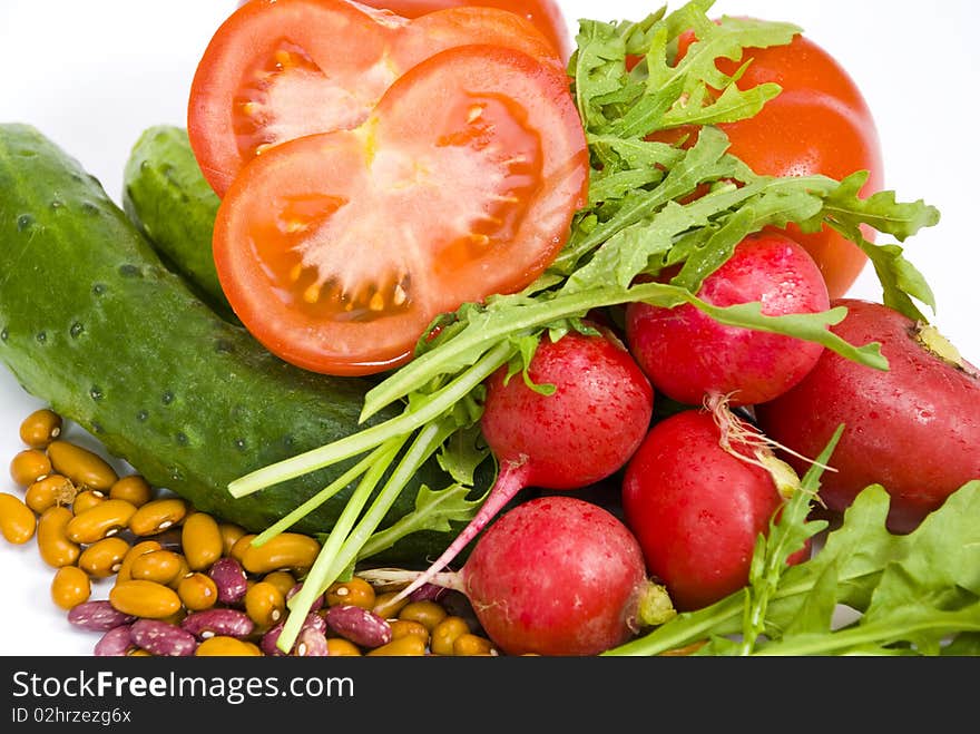 Fresh tomatoes, cucumbers, radishes, colorful beans and arugula on the white background, close-up, one tomato cut, all vegetables are coverd with drops of water. Fresh tomatoes, cucumbers, radishes, colorful beans and arugula on the white background, close-up, one tomato cut, all vegetables are coverd with drops of water.