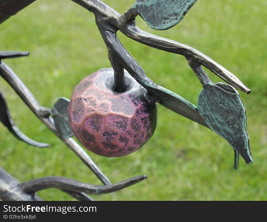 Metal forged branch with apples on a background lawn