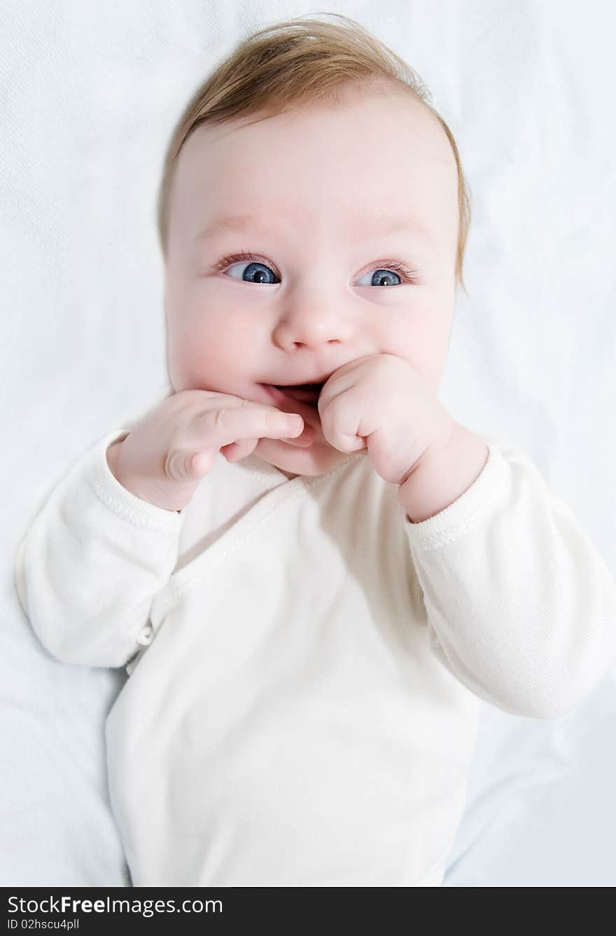 Adorable laughing baby boy lying with hands in his mouth