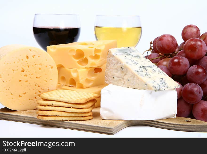 Various types of cheese (swiss, yellow, brie, blue cheese) with red and white wine, red grapes and crackers in close up on white background