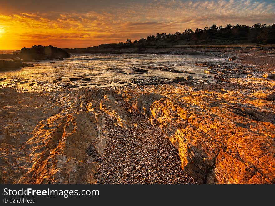 A rocky beach is cast in a gold glow from the setting sun by the Pacific Ocean. A rocky beach is cast in a gold glow from the setting sun by the Pacific Ocean