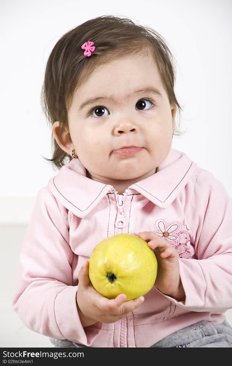 Sulky baby girl holding a green apple in her hands thinking and looking up.Check also Children. Sulky baby girl holding a green apple in her hands thinking and looking up.Check also Children