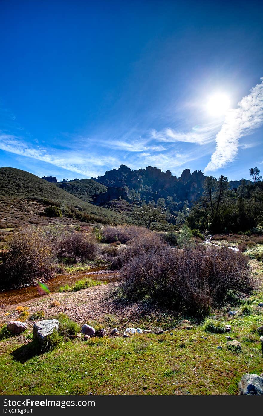 Mountain range in distance, grass and trees. Sky is filled with thine clouds and sun is out. Creek running across. Mountain range in distance, grass and trees. Sky is filled with thine clouds and sun is out. Creek running across