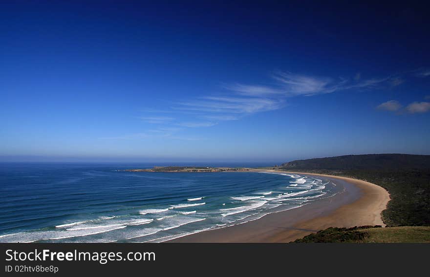 Landscape view of a deserted beach with rows of white breakers and a brilliant clear blue sky with an odd white cloud wisp. Landscape view of a deserted beach with rows of white breakers and a brilliant clear blue sky with an odd white cloud wisp