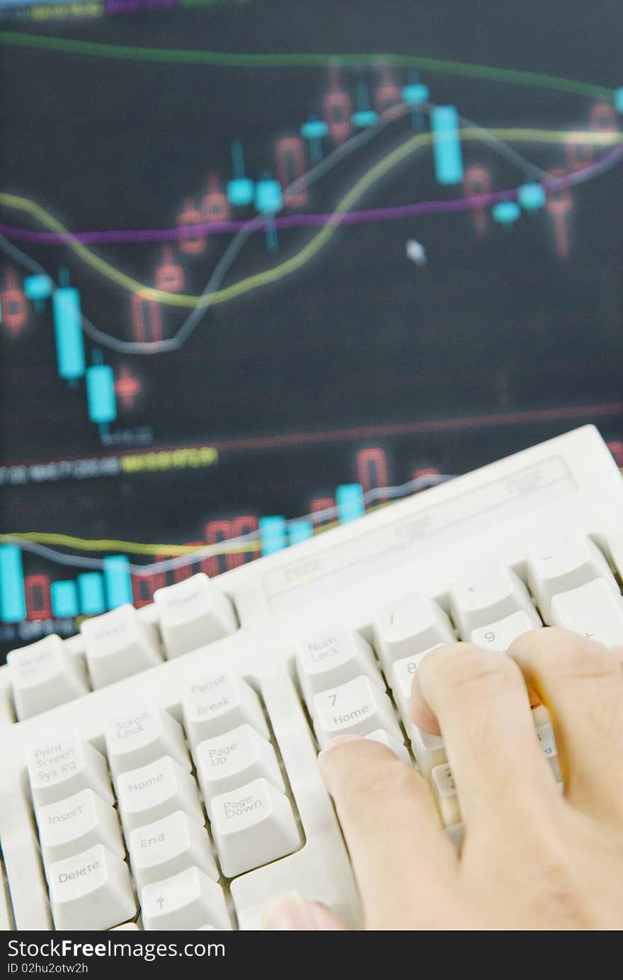 A hand operating keyboard , the background is the stock market graph