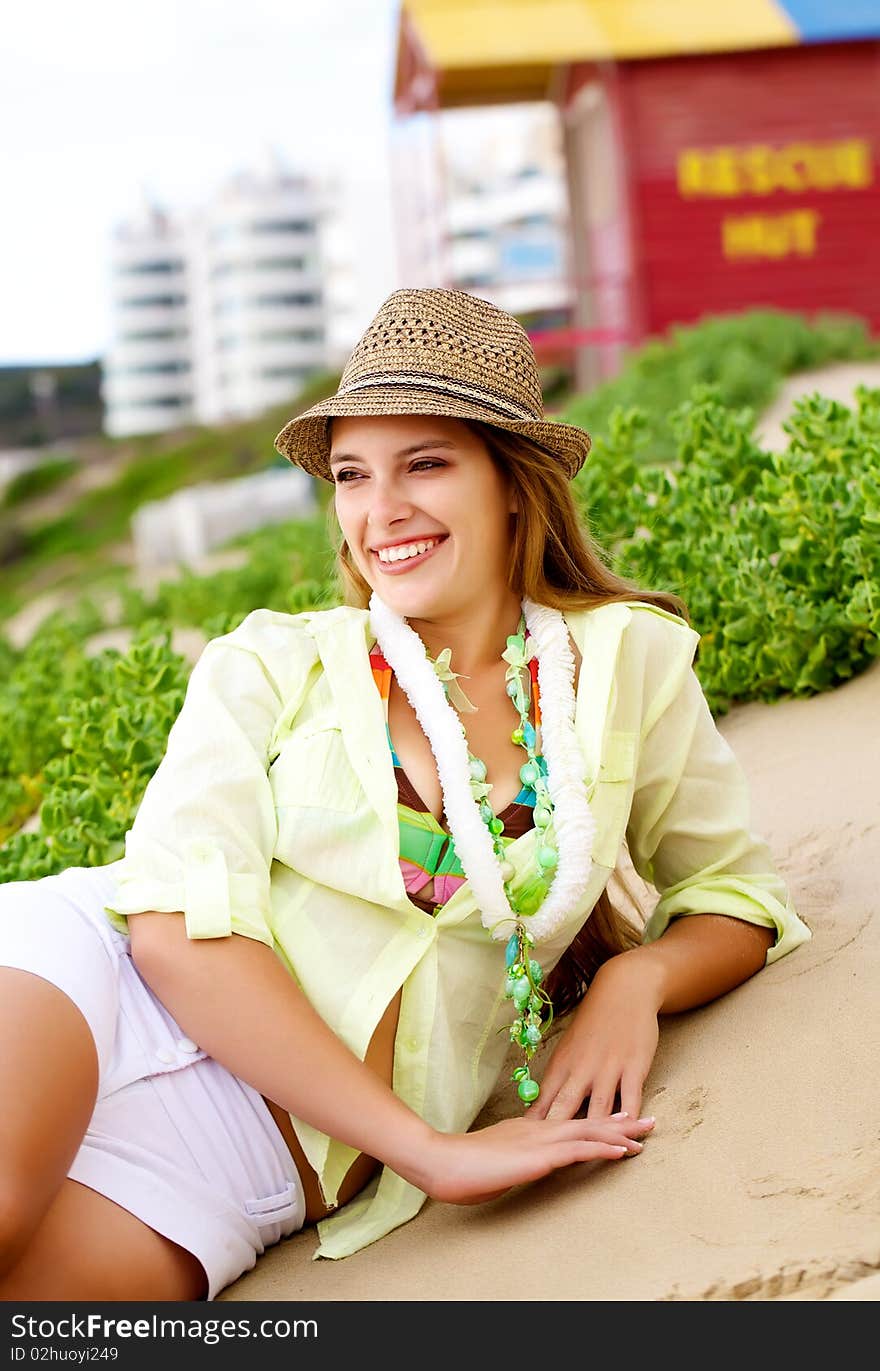 Attractive woman lying down on the sand wearing a hat with a red rescue hut in the background. Attractive woman lying down on the sand wearing a hat with a red rescue hut in the background.