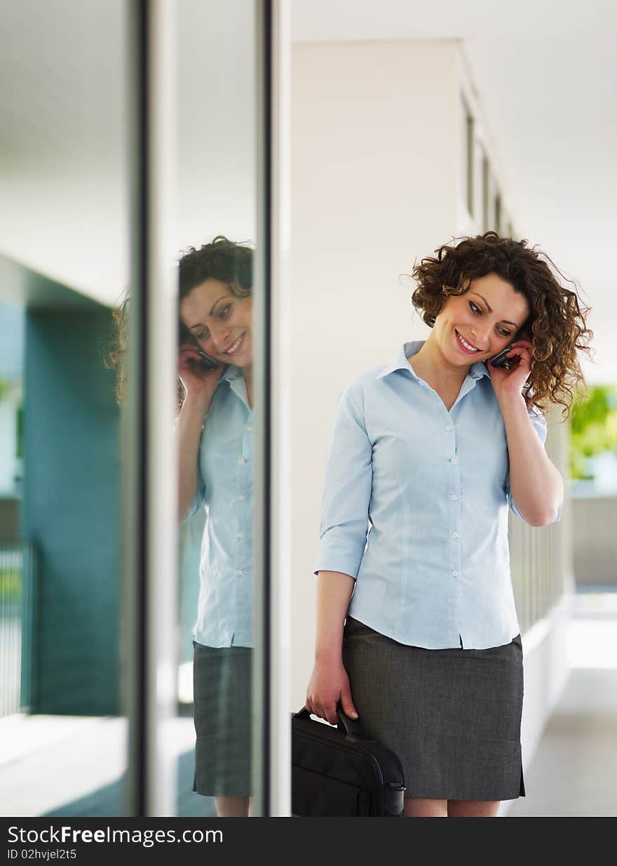 Italian business woman talking on mobile phone outdoors and smiling. Vertical shape, copy space. Italian business woman talking on mobile phone outdoors and smiling. Vertical shape, copy space