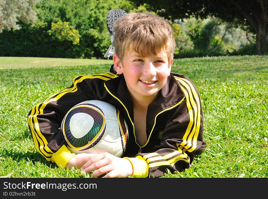 The boy hugged the ball, lying on the grass in the meadow in front of the photographer. The boy hugged the ball, lying on the grass in the meadow in front of the photographer