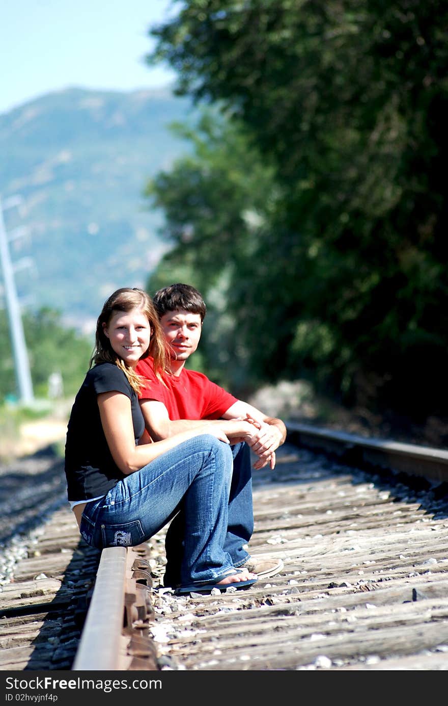 This is a photo of a couple holdings hands while sitting down on railroad tracks. This is a photo of a couple holdings hands while sitting down on railroad tracks.