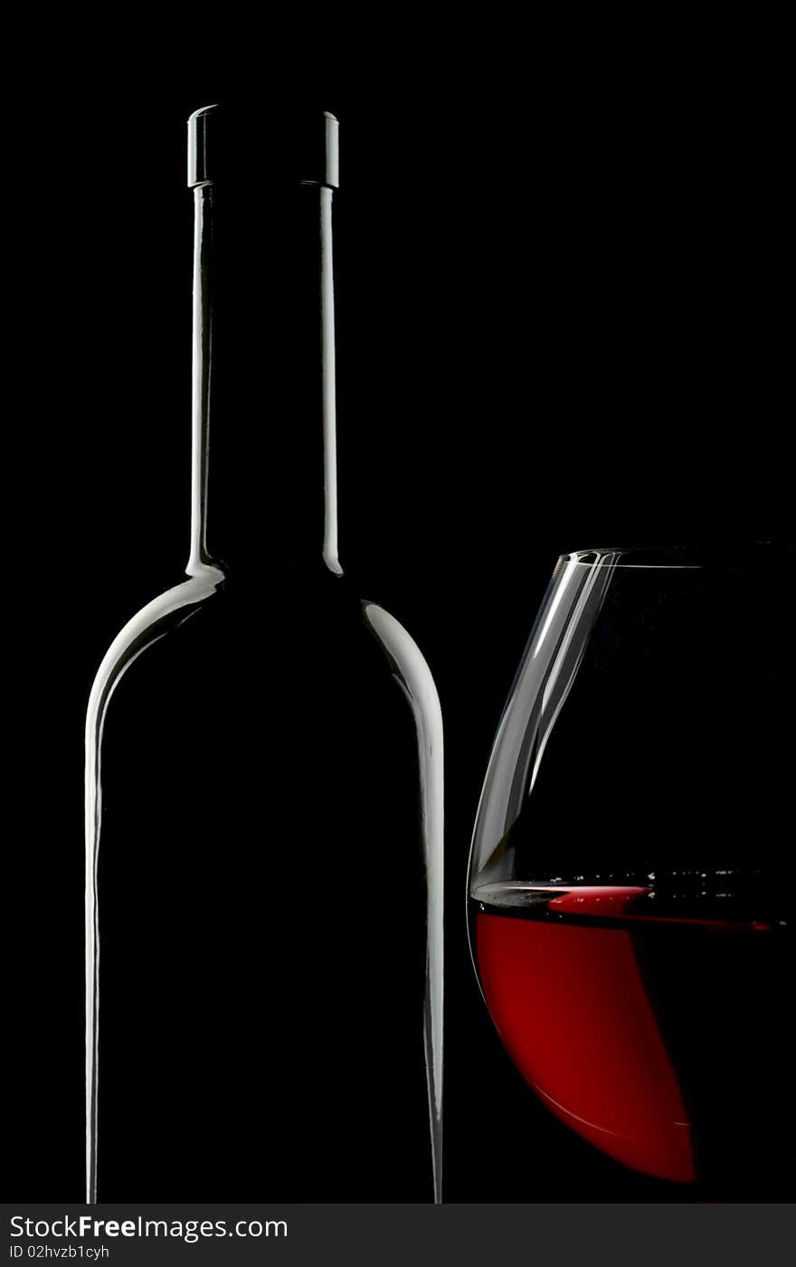 Bottle and glass of red wine over black background. Copy space on top.