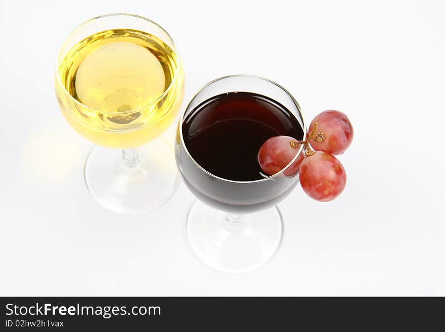 Red and white wine in wineglasses with three red grapes on white background