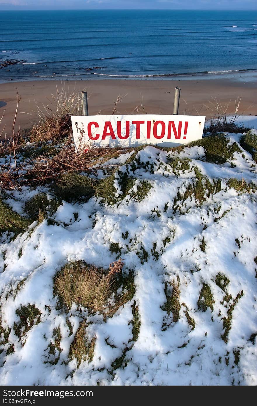 A red caution sign on a cliff edge in snow covered ballybunion. A red caution sign on a cliff edge in snow covered ballybunion