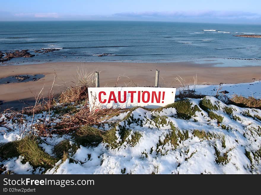 A red caution sign on a cliff edge in snow covered ballybunion. A red caution sign on a cliff edge in snow covered ballybunion