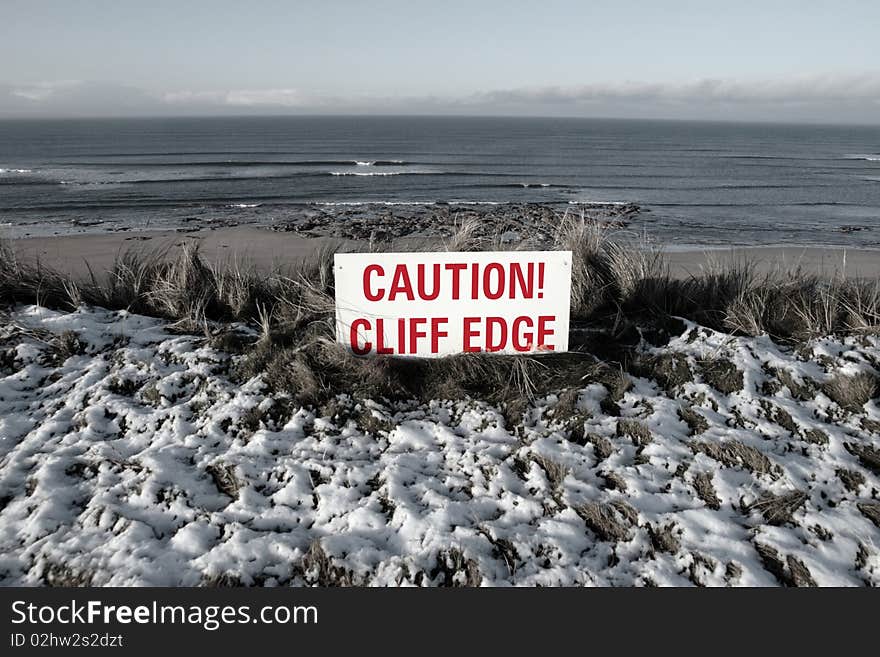 A red caution sign on a cliff edge in snow covered ballybunion. A red caution sign on a cliff edge in snow covered ballybunion