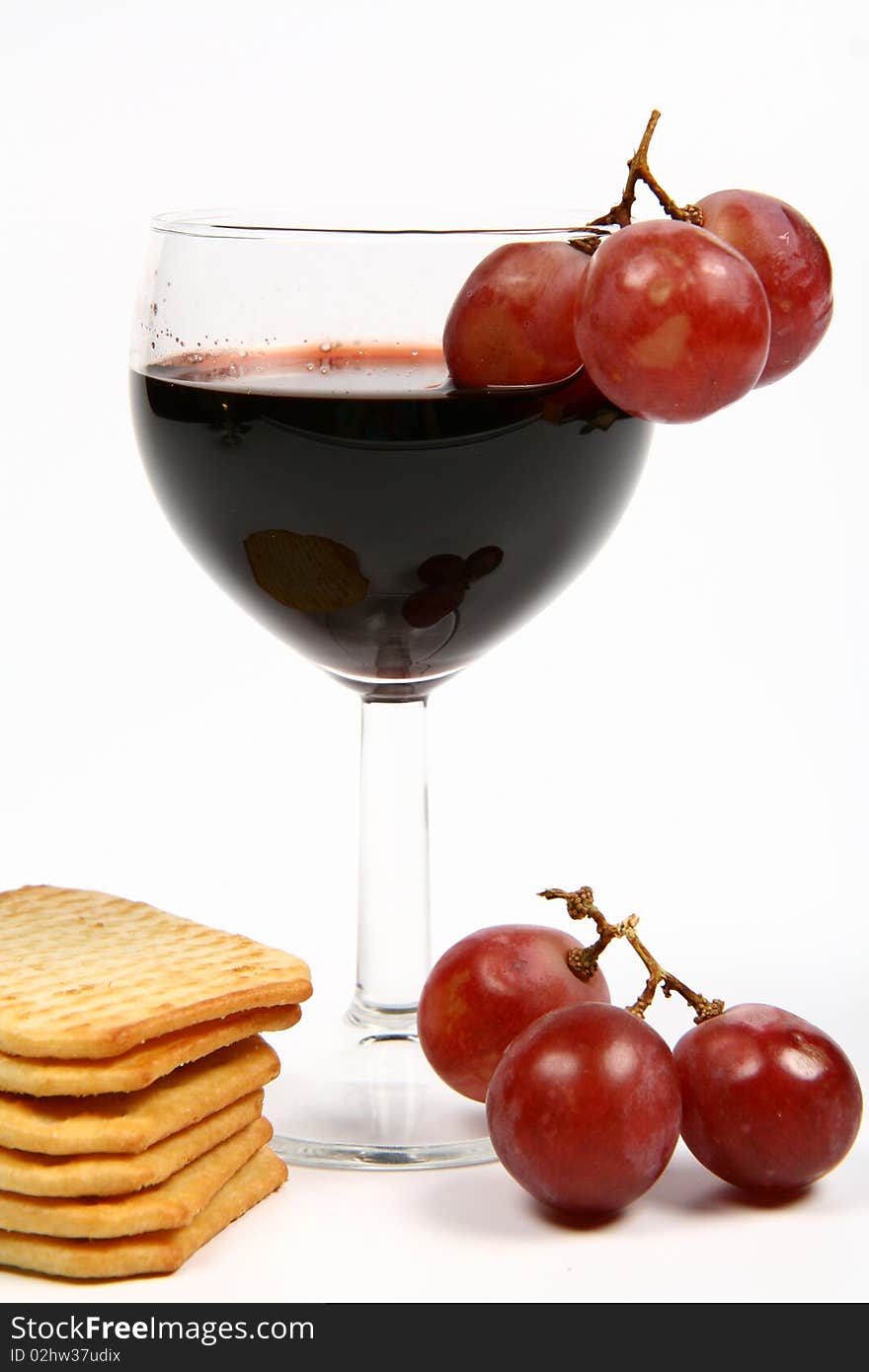 Red wine in a wineglass with red grapes and some crackers on white background