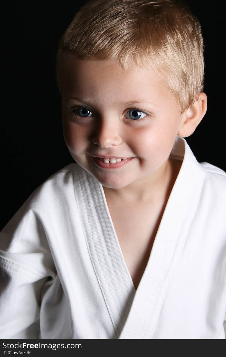 Young boy wearing his karate uniform on a black background. Young boy wearing his karate uniform on a black background