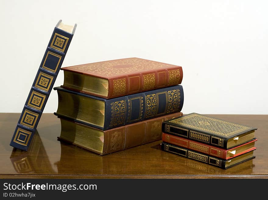 A pile of classic leather bound books with gold designs on the cover.