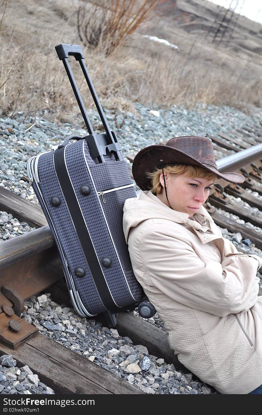 Young blond woman in a bright jacket sits on rails and is 
based on a large travel bag on wheels, cowboy style, bag with wheels tilted, a pen nominated. Young blond woman in a bright jacket sits on rails and is 
based on a large travel bag on wheels, cowboy style, bag with wheels tilted, a pen nominated