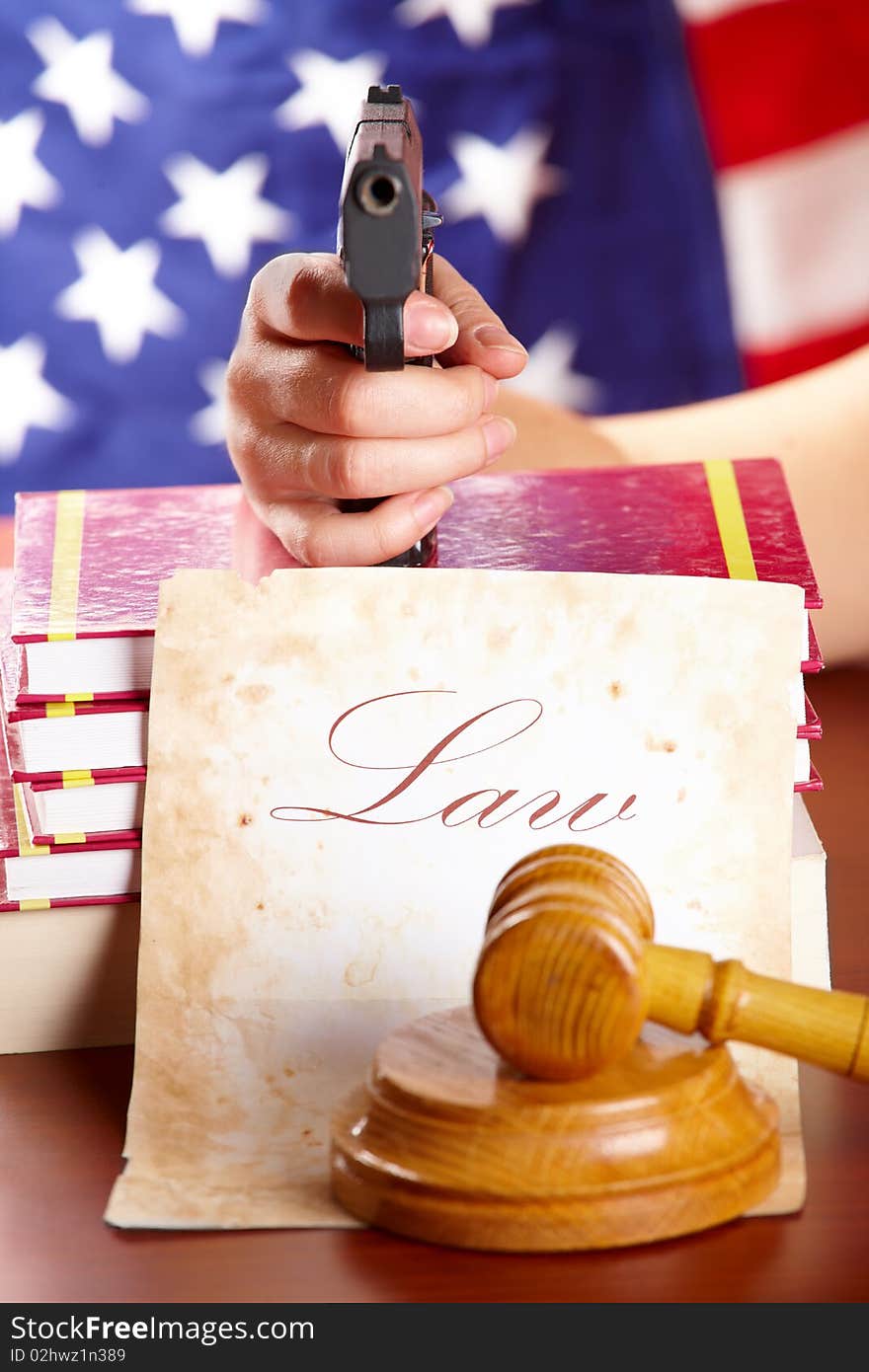 Hand with gun aiming at judges wooden gavel with gun and very old paper with US flag in the background. Hand with gun aiming at judges wooden gavel with gun and very old paper with US flag in the background