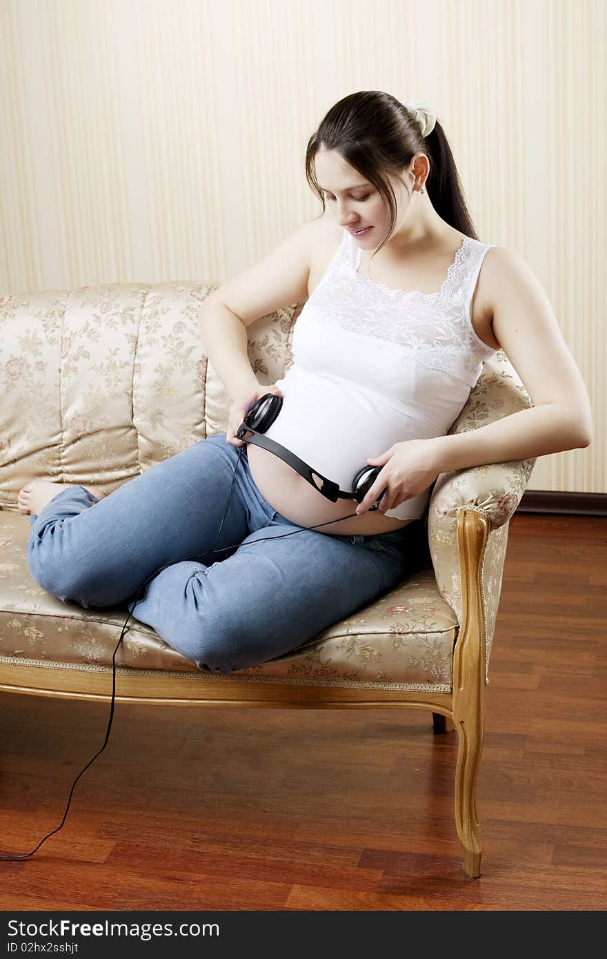 The image of a pregnant woman lying on the sofa and listening to music with headphones. The image of a pregnant woman lying on the sofa and listening to music with headphones