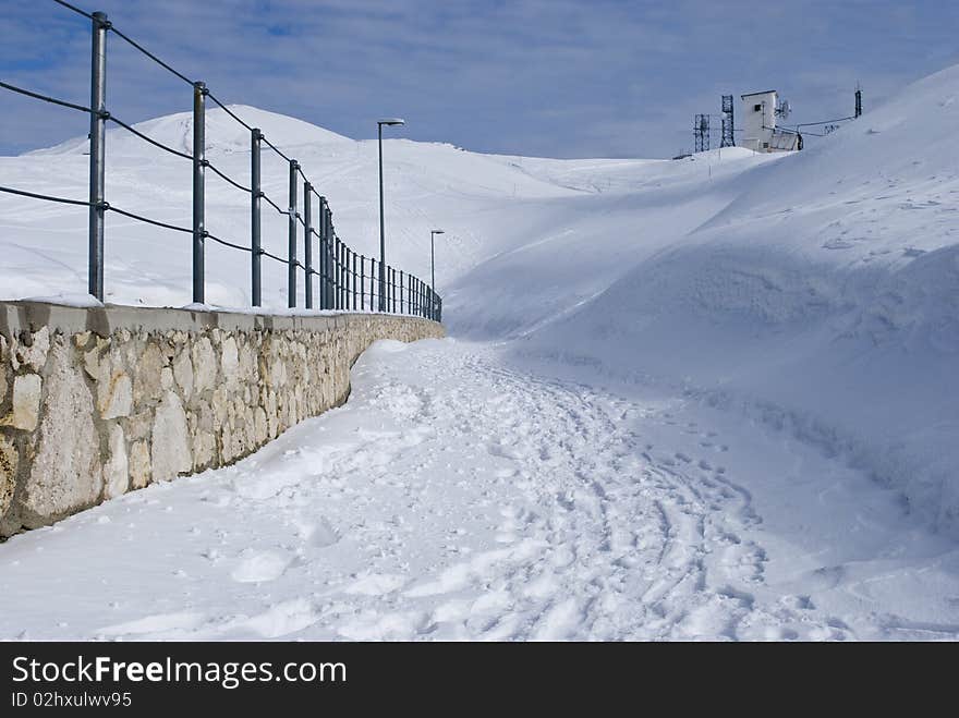 Snow path in mountains with a small brick wall. Snow path in mountains with a small brick wall