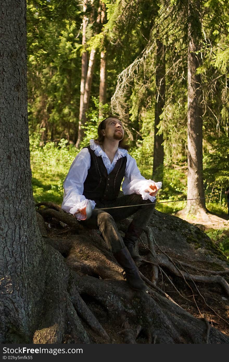 Man in historical costume sits on the roots of a tree