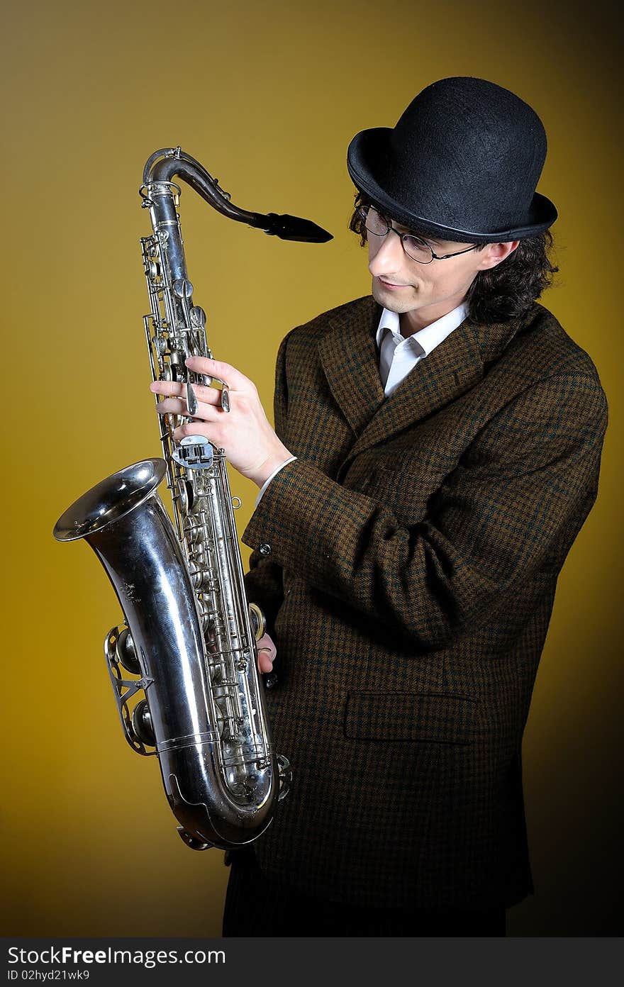 Portrait of young english gentleman in bowler hat holding saxophone. yellow background. Portrait of young english gentleman in bowler hat holding saxophone. yellow background