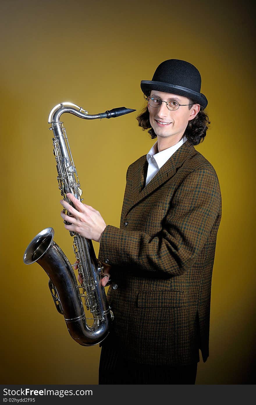 Portrait of young english gentleman in bowler hat holding saxophone. yellow background. Portrait of young english gentleman in bowler hat holding saxophone. yellow background