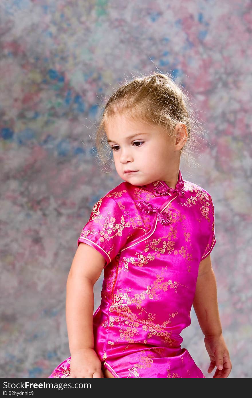 Portrait of a pretty little blond headed girl sitting on a stool looking back over her shoulder.  Painted background. Portrait of a pretty little blond headed girl sitting on a stool looking back over her shoulder.  Painted background.