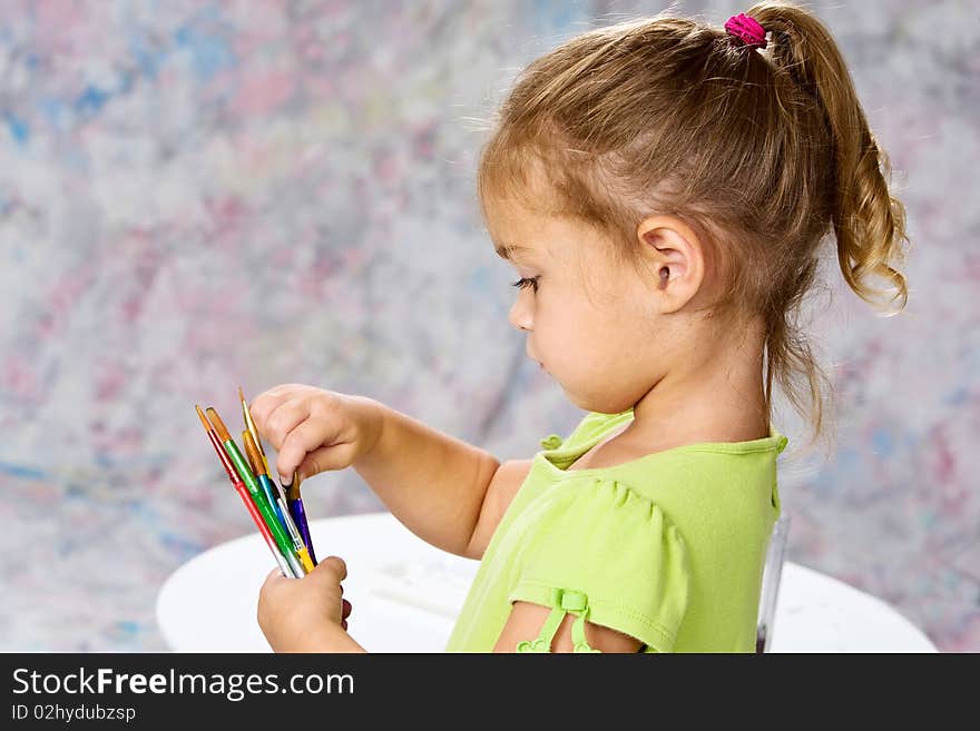 Cute little girl in green blouse picking out the right water color brush for her painting. Cute little girl in green blouse picking out the right water color brush for her painting.