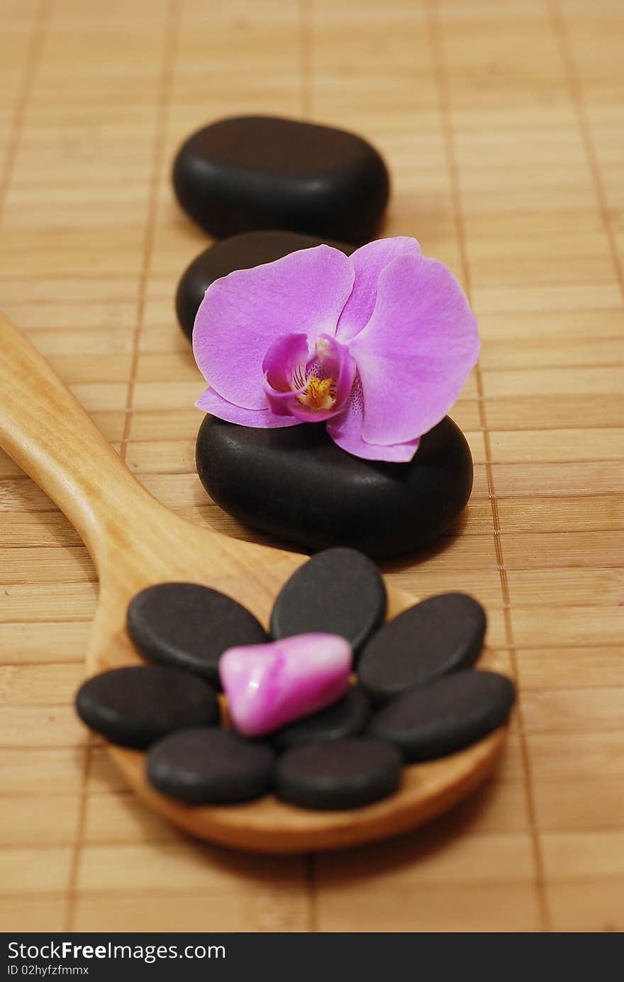 Wooden spoon with stones and the flower of the orchid on the bamboo mat. Wooden spoon with stones and the flower of the orchid on the bamboo mat