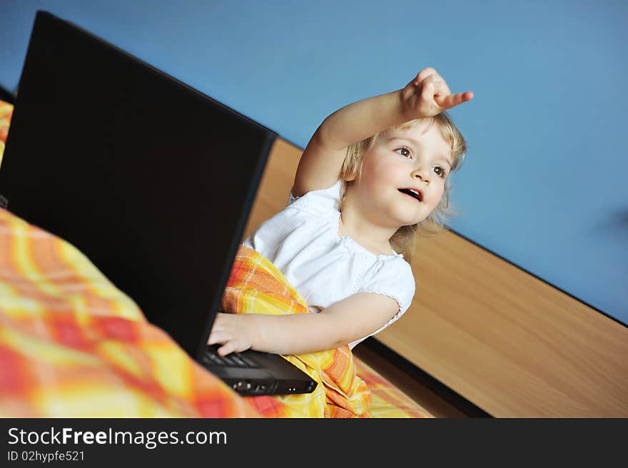 Cheerful little girl with laptop sits on bed of parents